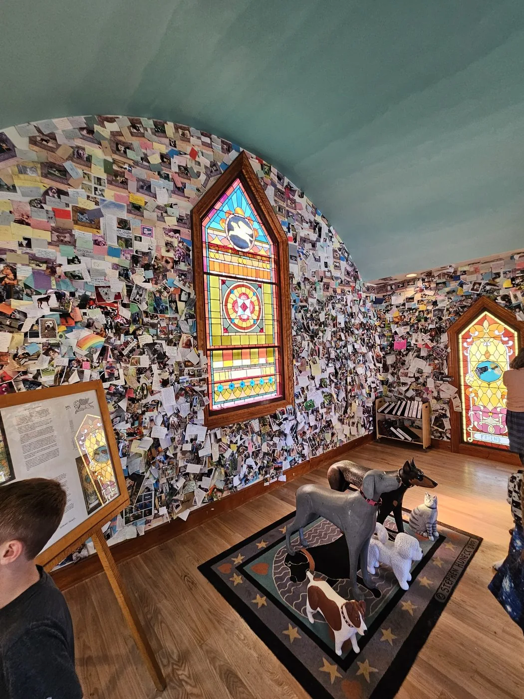 Inside the Dog Chapel: every wall covered from floor to arched ceiling with thumbtacked photographs and handwritten notes, surrounding a stained glass window.